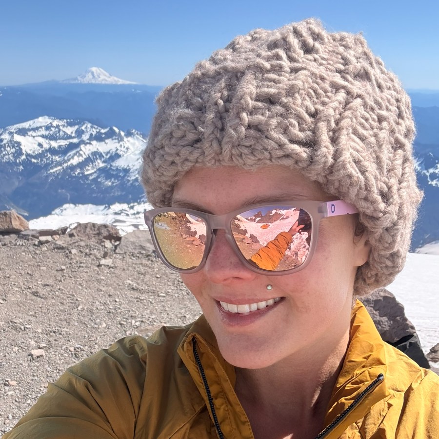 Hannah Grossman smiling on a snowy summit, a distant volcano over her shoulder