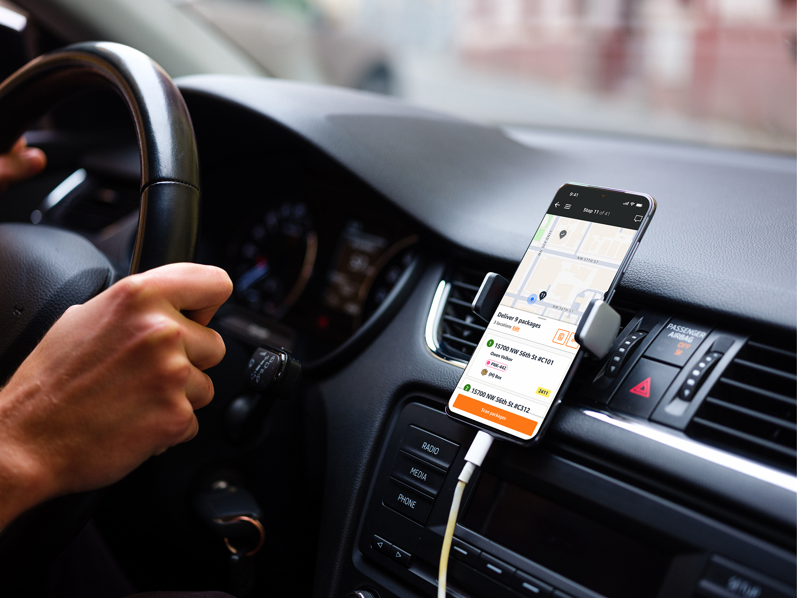 A driver at the wheel with the Amazon delivery app showing a grouped stop on a dash-mounted phone