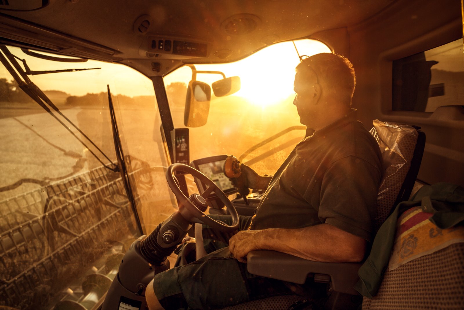 A producer in a combine cab at sunset, dashboard screens glowing against the low sun