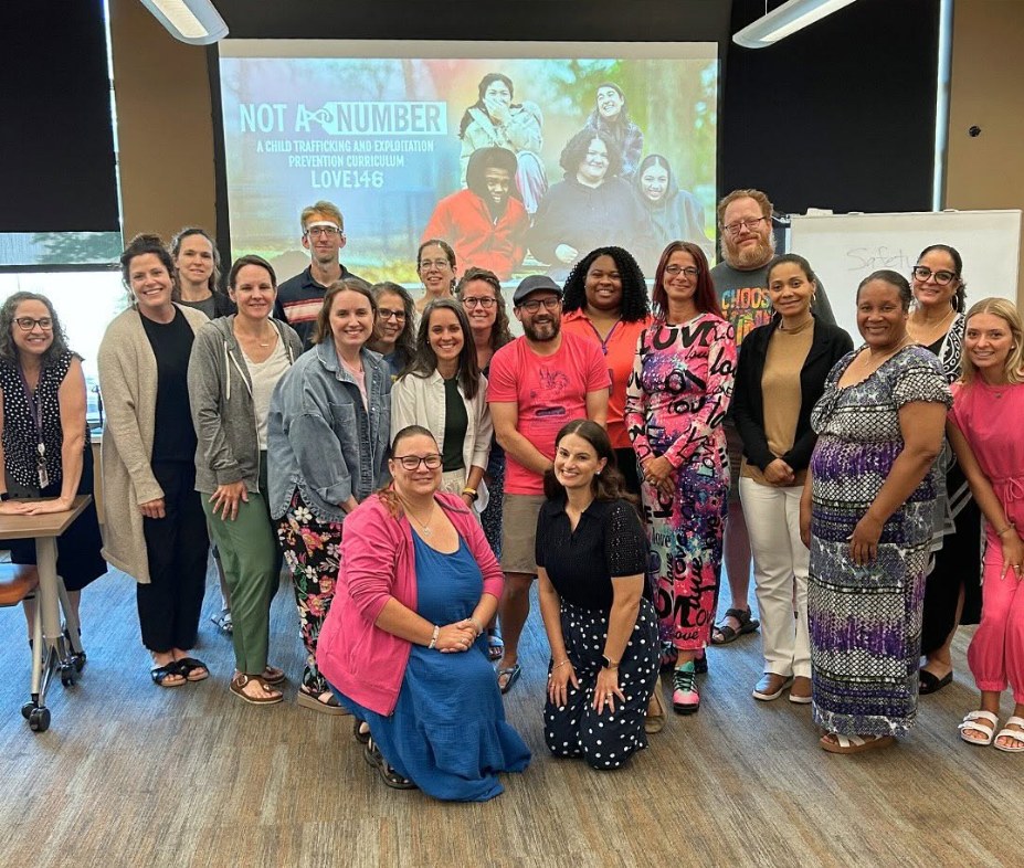 A room of Not a #Number facilitators at a training, the curriculum title slide projected behind them